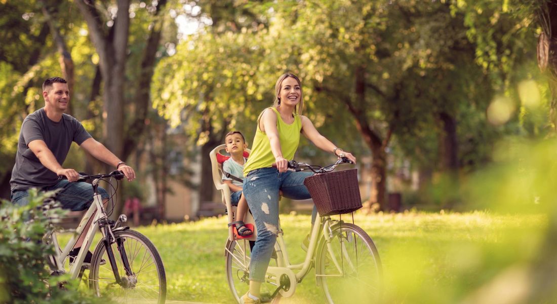 Smiling active father and mother with kid on bicycles having fun in park.